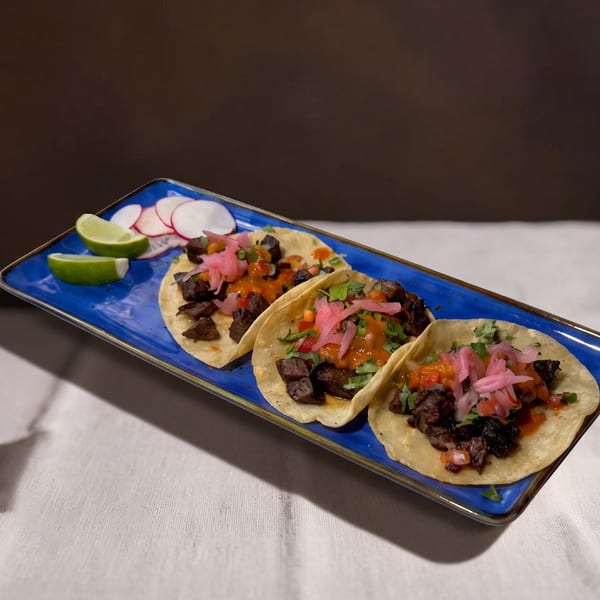 Three carne asada street tacos with pickled onions, cilantro, and salsa on a blue plate.