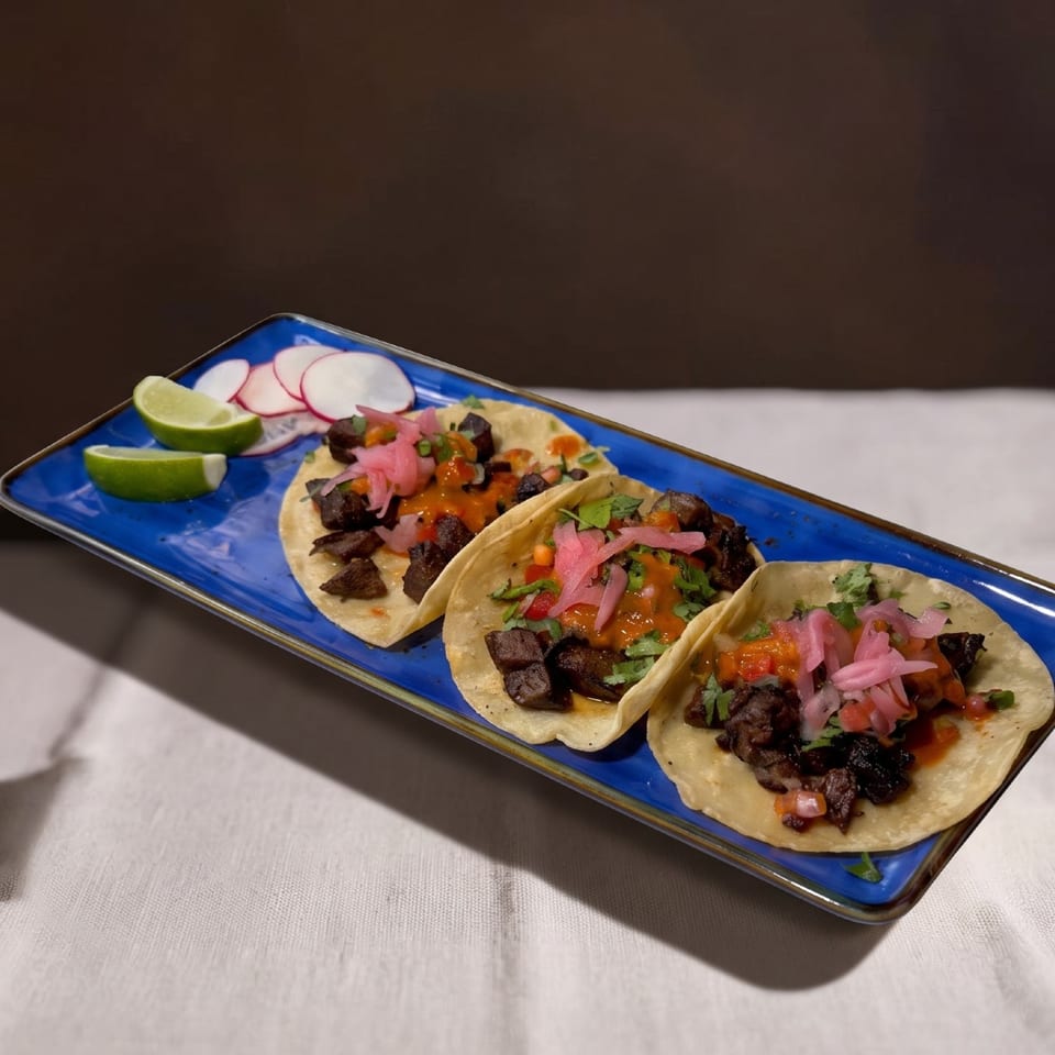 Three carne asada street tacos with pickled onions, cilantro, and salsa on a blue plate.