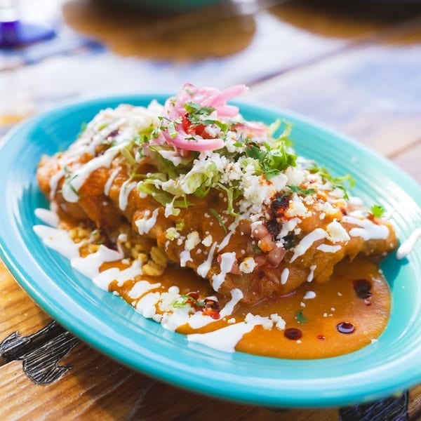 Mexican dish with red sauce, crumbled cheese, lettuce, and pickled onions on a turquoise plate.